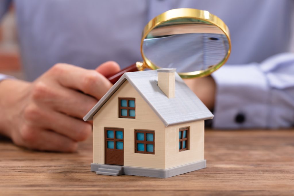 Man Holding Magnifying Glass Over House Model